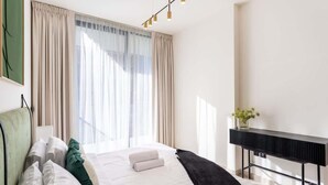 A hotel room with a bed, curtains, a bedside table with a vase, and a modern light fixture.