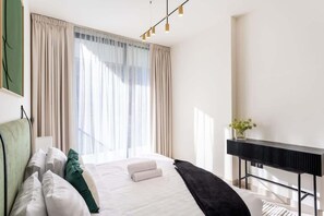 Habitación de hotel con cama, cortinas, mesita de noche con un florero y una lámpara moderna.