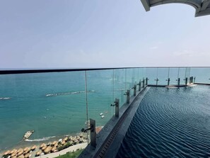 Una piscina con fondo de cristal que ofrece vistas infinitas a un cuerpo de agua con un muelle y barcos.