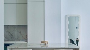 Una cocina moderna con dos taburetes de bar, encimera de mármol y muebles de color blanco.