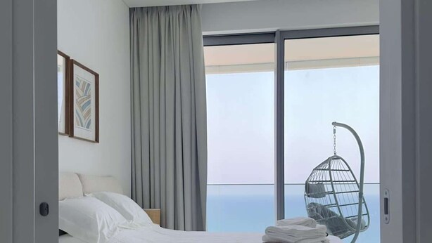 Un dormitorio moderno con una cama grande, un sillón colgante y vistas al océano.