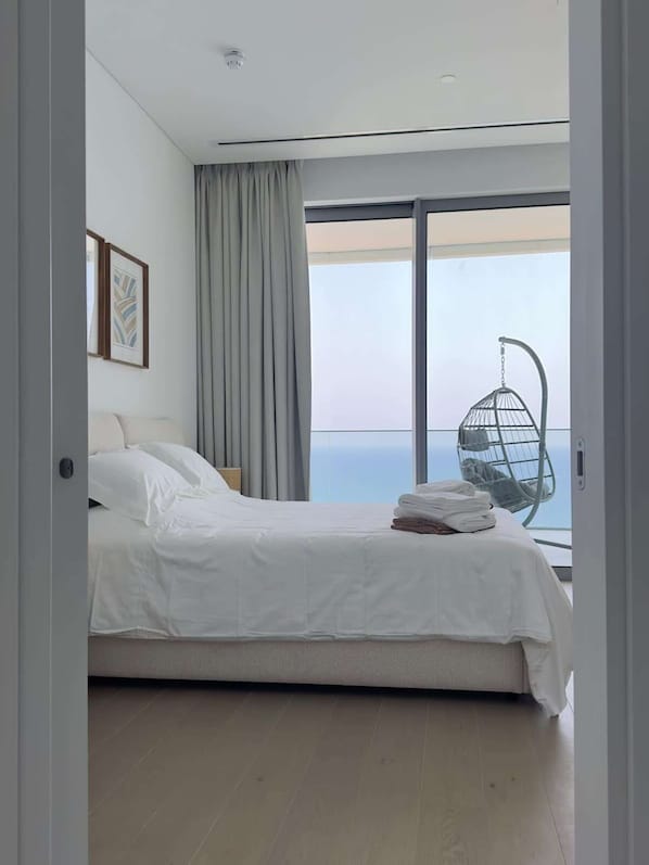 Un dormitorio moderno con una cama grande, un sillón colgante y vistas al océano.