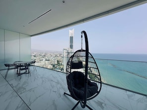 Varanda com cadeira suspensa, uma mesa e vista para a cidade.