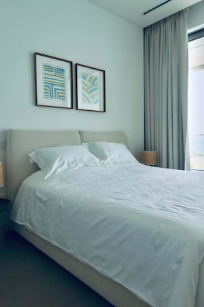 Quarto de hotel com uma cama, duas pinturas abstratas emolduradas, uma janela com cortinas e um abajur.