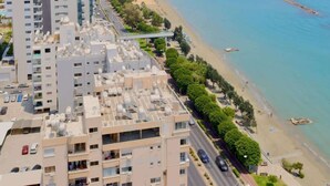 Un edificio de gran altura con diseño moderno, junto a una playa de aguas azules cristalinas y algunas embarcaciones.