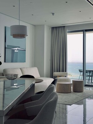 Una sala de estar moderna con una mesa de comedor de vidrio, asientos cómodos, un ventanal con vista al mar y un diseño minimalista.