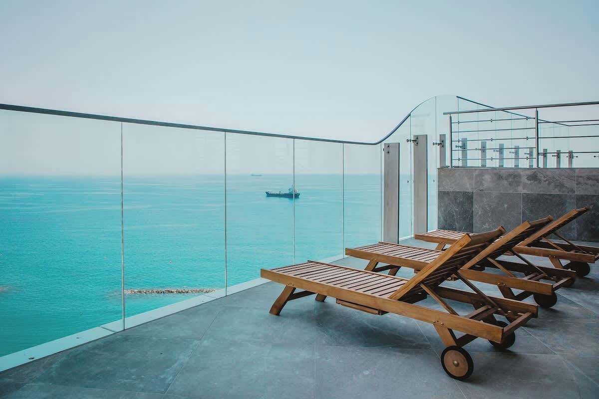 Ein Balkon mit Meerblick, Holzliegen und einem Glasgeländer.