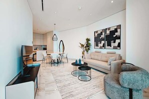 Una sala moderna con un sofá, una mesa de centro y un televisor. Hay un comedor con sillas y una mesa. La habitación tiene un diseño minimalista, un ventanal grande y obras de arte en la pared.