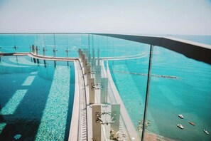 Una piscina infinita con paredes de vidrio, agua azul cristalina, un deck curvo y vistas al mar.