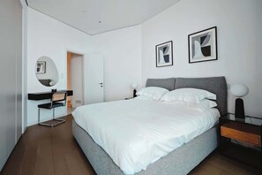 Un dormitorio moderno con una cama grande, una mesita de noche, una silla y un escritorio con espejo.