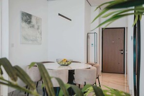Ein moderner Essbereich mit einem runden Tisch, Stühlen und einer Obstschale. Im Vordergrund befindet sich eine Tür und eine Pflanze.
