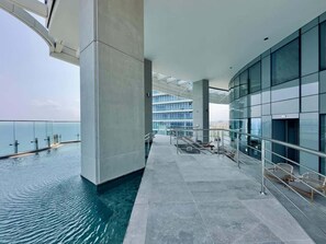 A modern infinity pool with a glass barrier, a clear sky, and a view of the sea. - Luxury Seafront Apt W Sea Views Pool & Gym (Limassol)