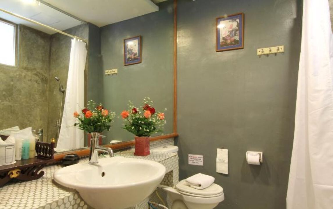 A bathroom with a sink, mirror, toilet, and shower curtain. There are two flower arrangements on the wall.