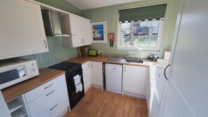 Una cocina compacta con armarios blancos, estufa, lavavajillas y ventana con vista a una casa.
