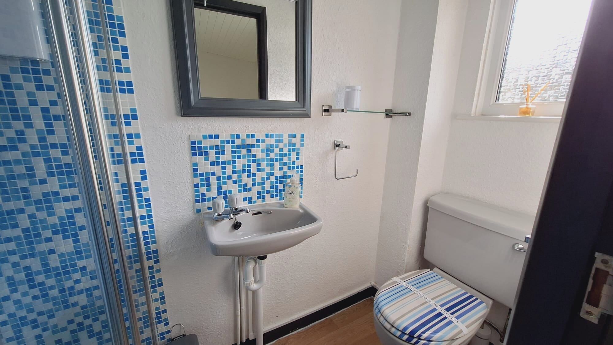 Une salle de bain avec un lavabo blanc, un miroir et des toilettes dont l’abattant est à rayures.