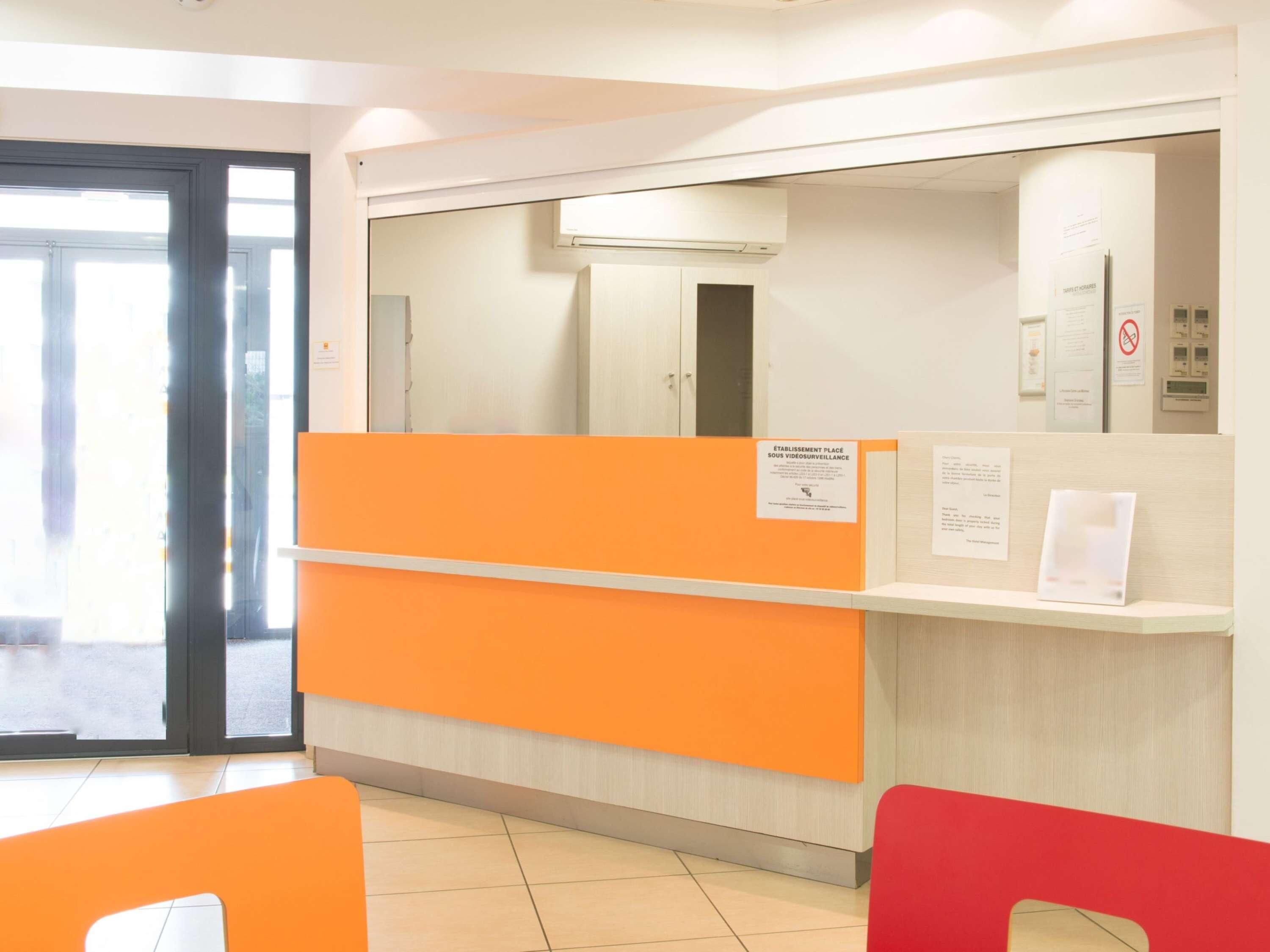 Un espace d’accueil avec un comptoir orange, une porte d’entrée en verre et un climatiseur fixé au mur.