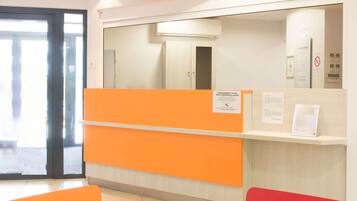 Un espace d’accueil avec un comptoir orange, une porte d’entrée en verre et un climatiseur fixé au mur.