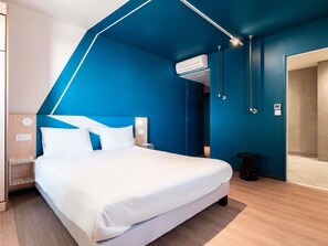Una habitación de hotel moderna con una cama grande, aire acondicionado integrado y una puerta de baño visible.