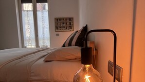 Un dormitorio con cama, mesita de noche con lámpara y ventana con cortinas.
