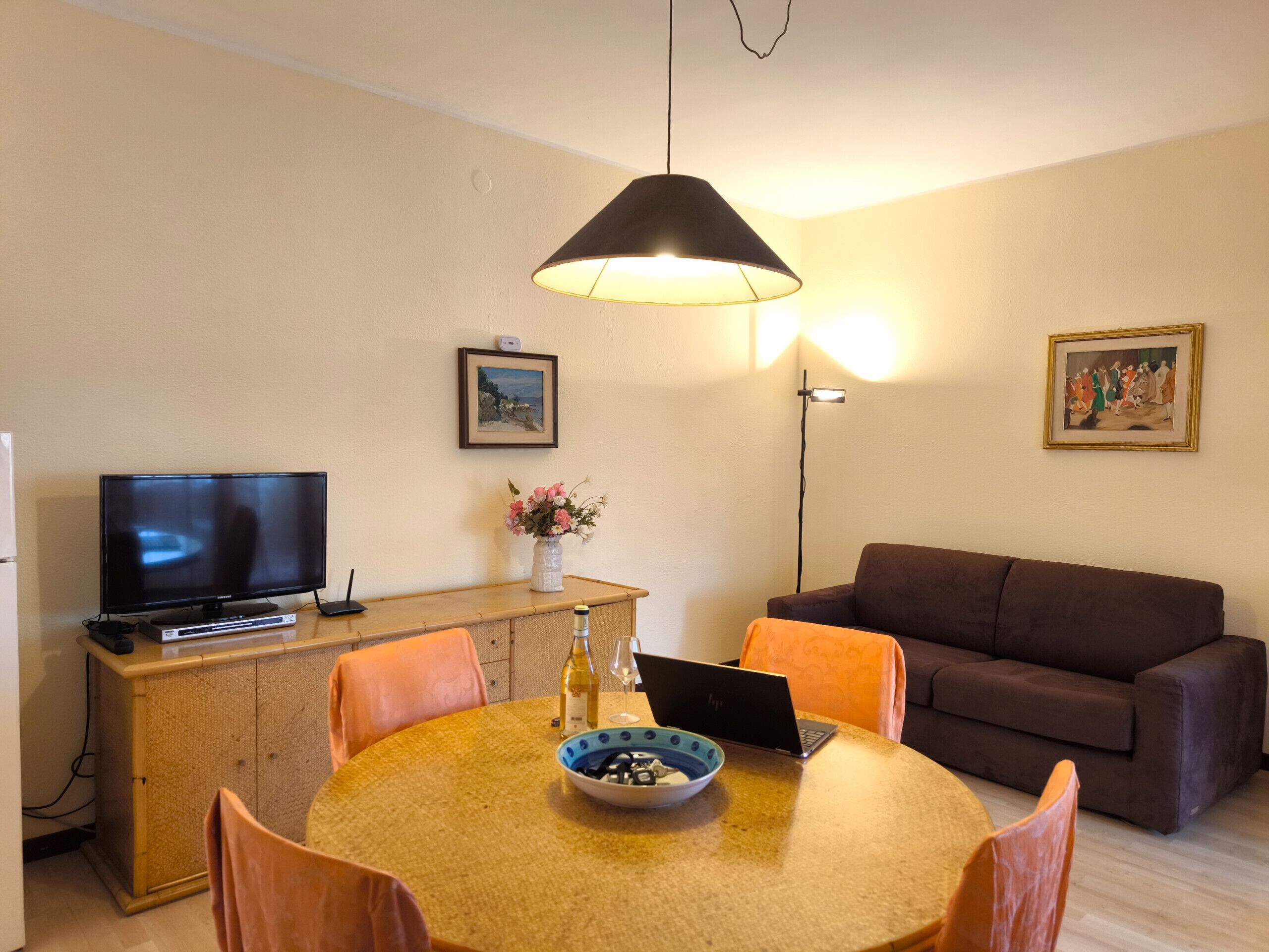 Un salon avec une table ronde en bois, un canapé marron, un téléviseur et un ordinateur portable.