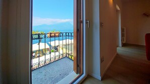 A room with a sliding glass door leading to a balcony with a view of the sea and mountains.