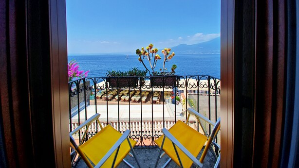 A balcony with yellow chairs, a view of the sea, and a distant sailboat.