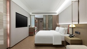 A modern hotel room with a large bed, bedside table with a lamp, a flat-screen TV mounted on the wall, and a wardrobe with a mirror. - Ramada Encore by Wyndham Kunming Jingkai (Kunming)