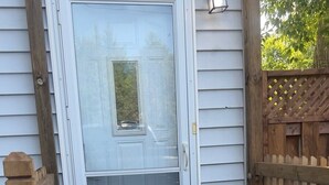 Une terrasse en bois avec une porte, un pot de fleurs et un paillasson.