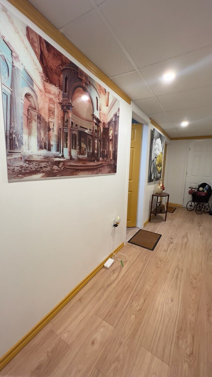 A hallway with wooden flooring, a large mural on the left wall, and a door at the end.