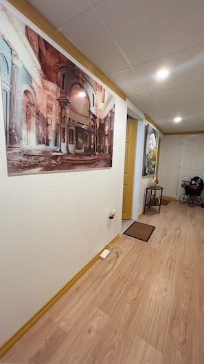 A hallway with wooden flooring, a large mural on the left wall, and a door at the end.