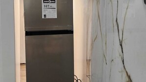 Un réfrigérateur compact et moderne, doté d’une étiquette indiquant sa consommation énergétique, est installé dans un couloir étroit aux murs de marbre et au plancher en bois.