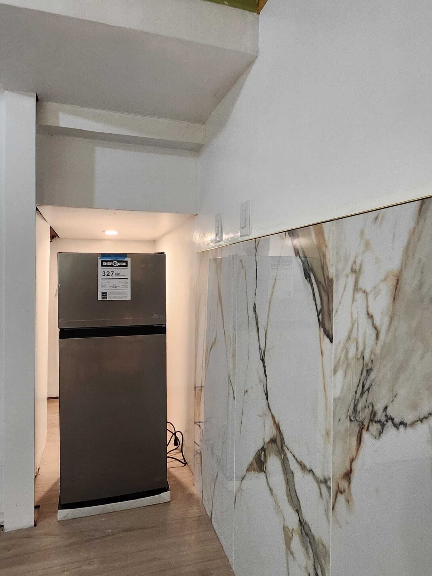 A hallway with a marble wall and a stainless steel refrigerator.