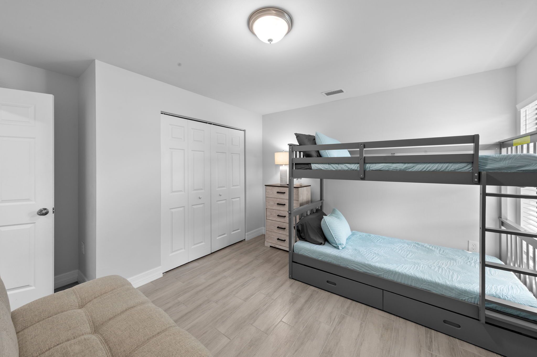 A bedroom with a bunk bed, a dresser, a door, and a light fixture.