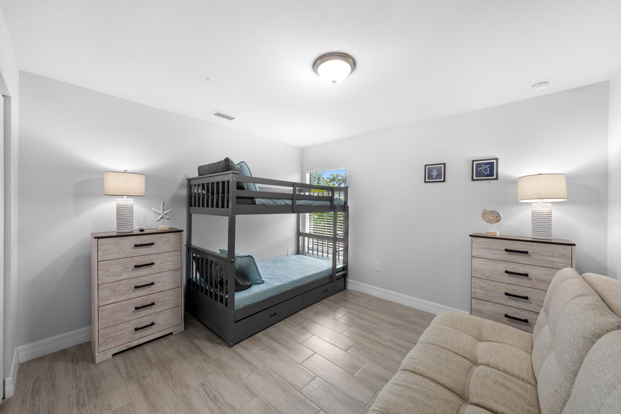 A bunk bed with a desk and drawers, a lamp, and a couch in a room with white walls and wooden flooring.