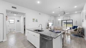 Cocina moderna con encimeras de granito, electrodomésticos de acero inoxidable y zona de comedor con sofá y mesa.