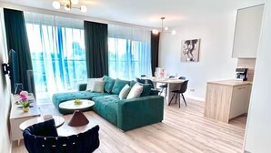 Un salon moderne avec un canapé vert, une table basse ronde et un coin repas comprenant une table et des chaises blanches.