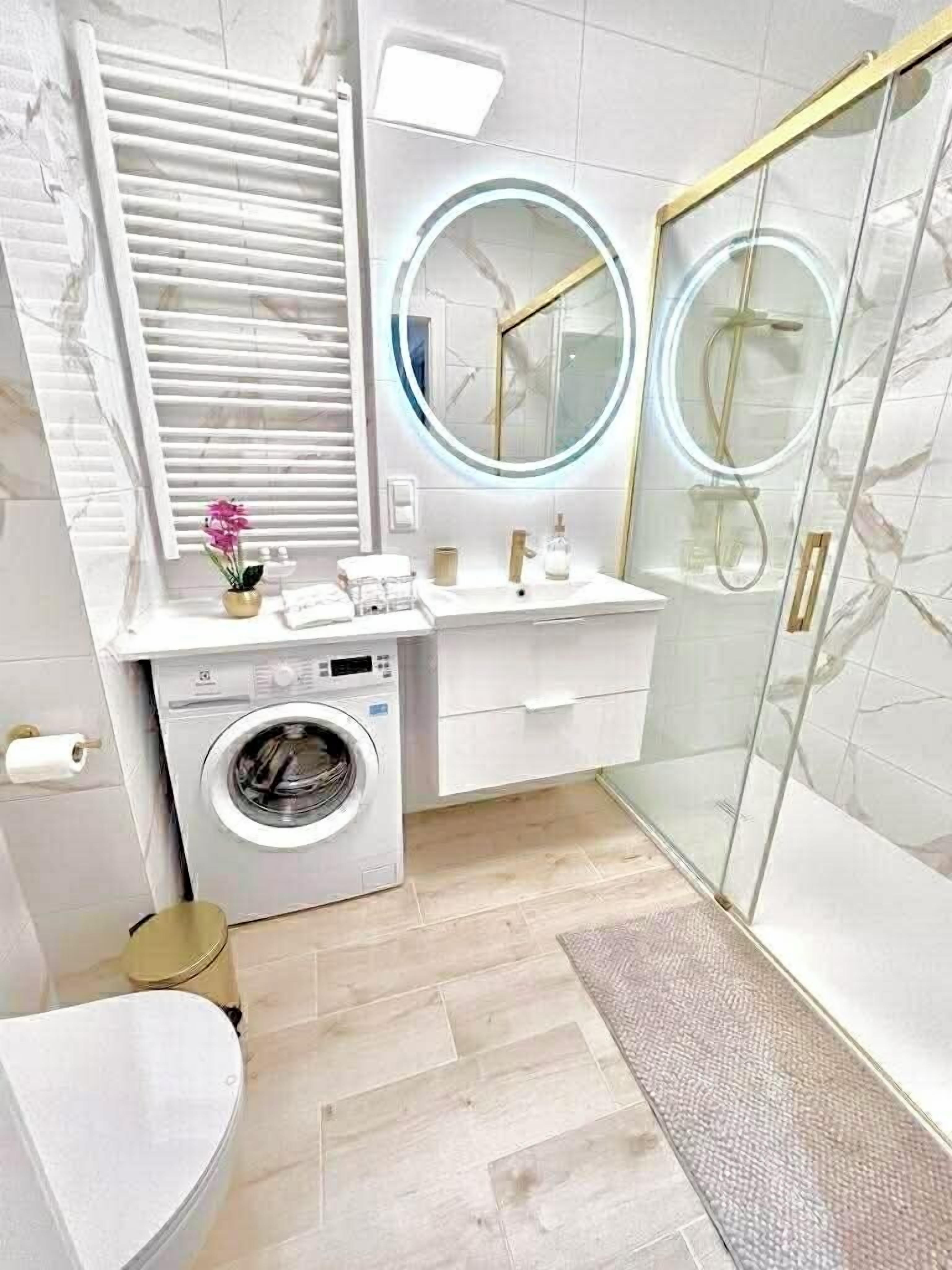 Une salle de bain moderne équipée d’un lave-linge, d’une douche à parois de verre et d’un meuble-lavabo avec un miroir rond.