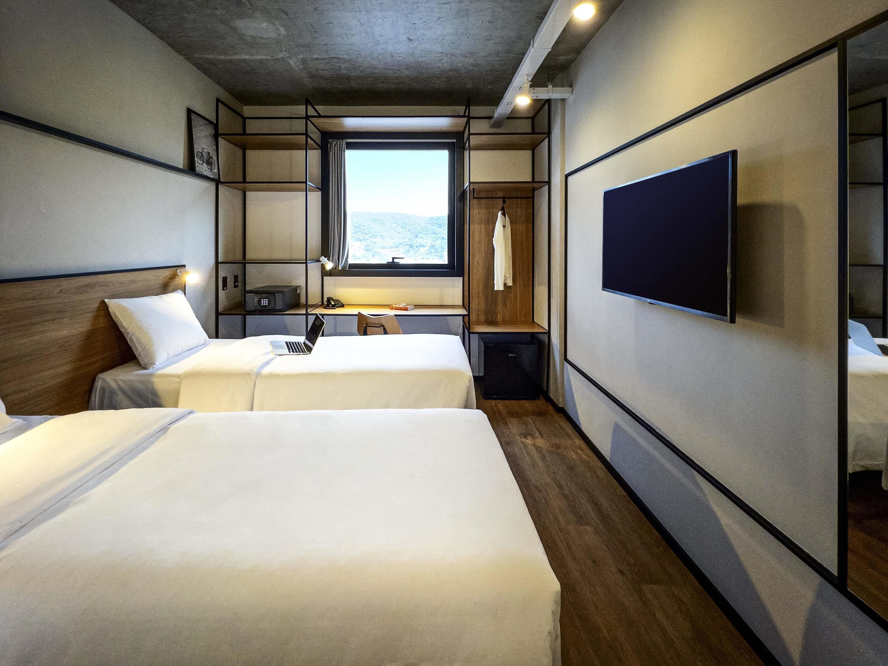 A hotel room with two beds, a desk with a chair, a TV, and a window with a view.