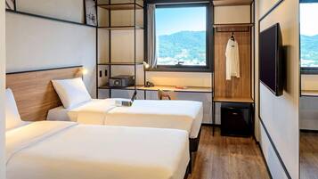 Habitación de hotel con dos camas, un escritorio, una silla, un televisor y una ventana con vistas a las montañas.