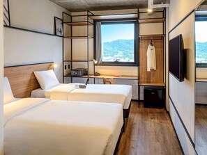 A hotel room with two beds, a desk, a chair, a TV, and a window with a view of the mountains.