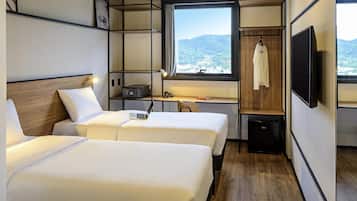 Habitación de hotel con dos camas, un escritorio, un televisor y una ventana con vista a las montañas.