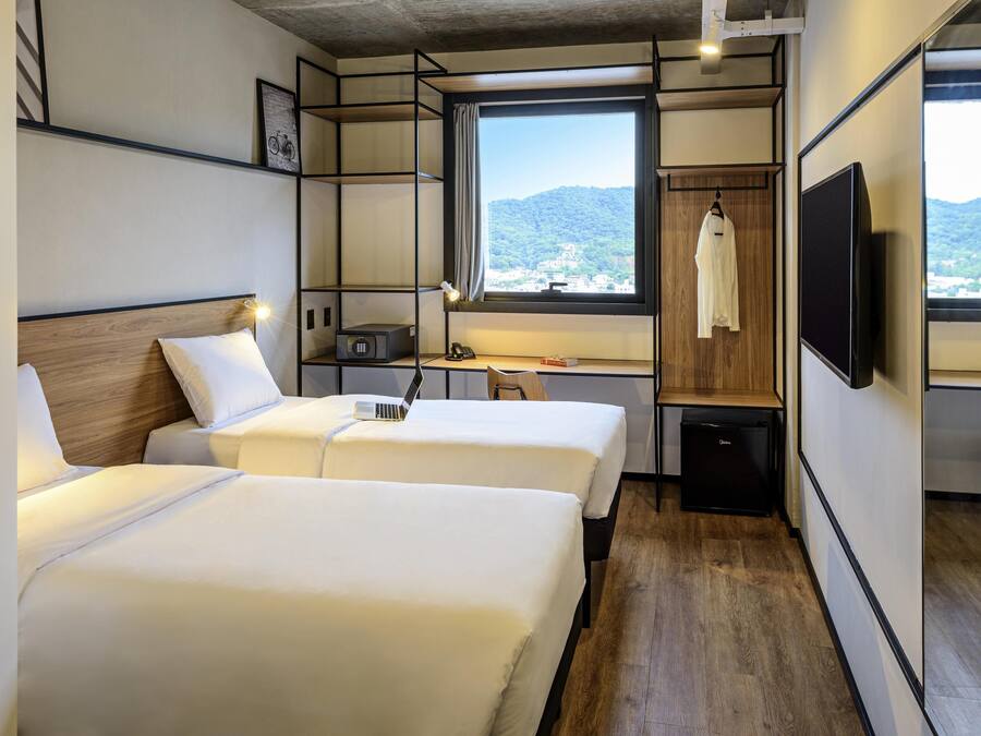 Habitación de hotel con dos camas, un escritorio, un televisor y una ventana con vista a las montañas.