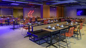Un comedor amplio con varias mesas y sillas, que presenta un diseño industrial moderno con techos y luminarias a la vista.