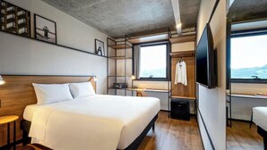 A modern hotel room with a large bed, a desk, a TV, and a view of the outdoors. - Ibis Balneario Camboriu (Balneário Camboriú)
