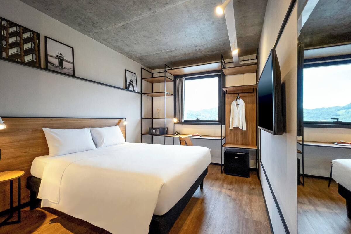 A modern hotel room with a large bed, a desk, a TV, and a view of the outdoors.
