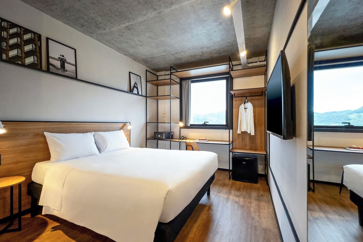 Ein modernes Hotelzimmer mit einem großen Bett, einem Schreibtisch, einem Fernseher und Blick ins Freie.
