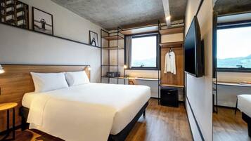 Habitación de hotel moderna con una cama grande, un escritorio, un televisor y vistas al exterior.