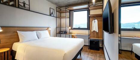Une chambre d’hôtel moderne, dotée d’un grand lit, d’un bureau, d’une télévision et offrant une vue sur l’extérieur.