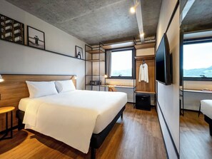 Ein modernes Hotelzimmer mit einem großen Bett, einem Schreibtisch, einem Fernseher und Blick ins Freie.