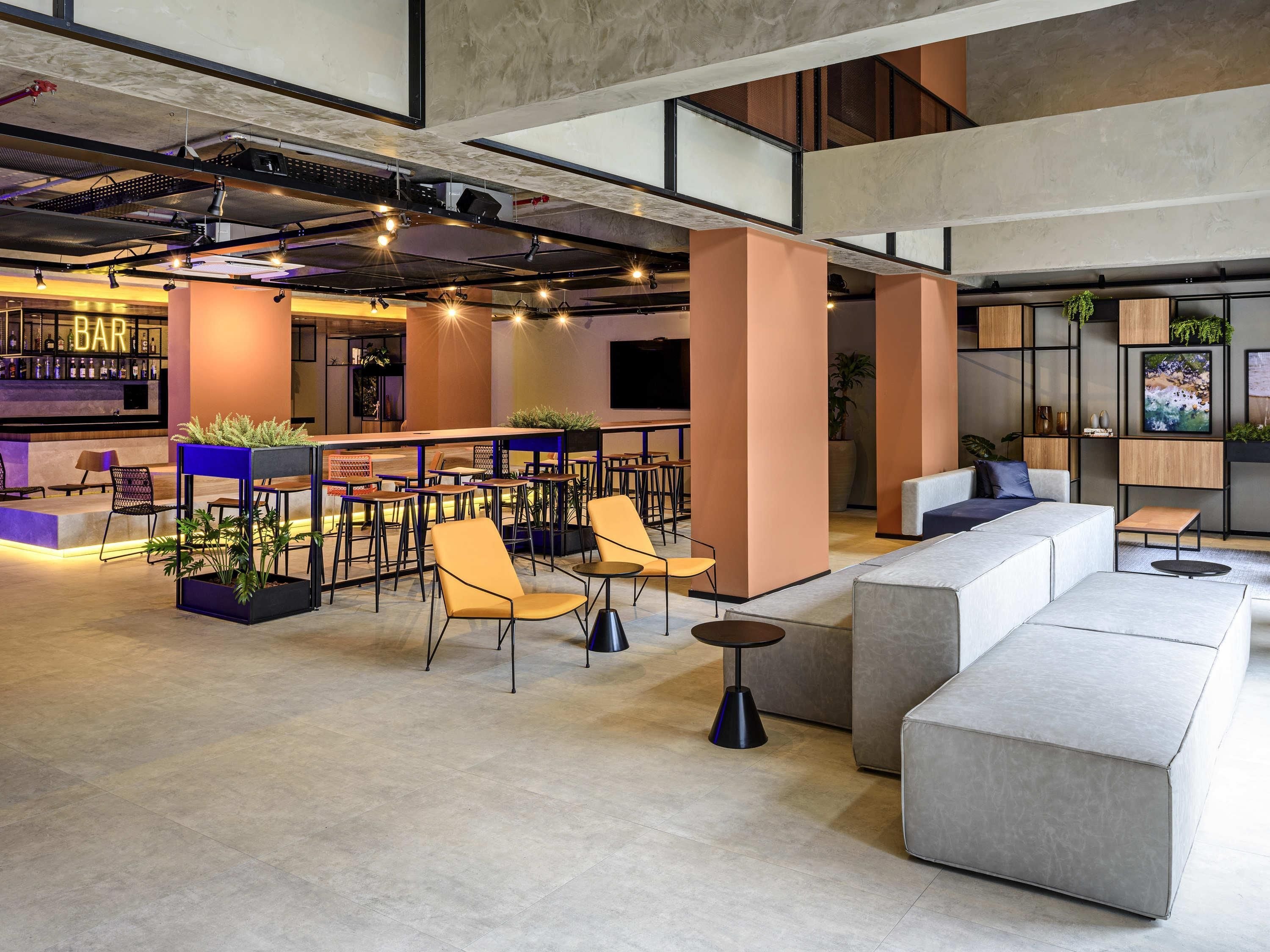 A modern lounge area with seating, a bar, and a large screen.